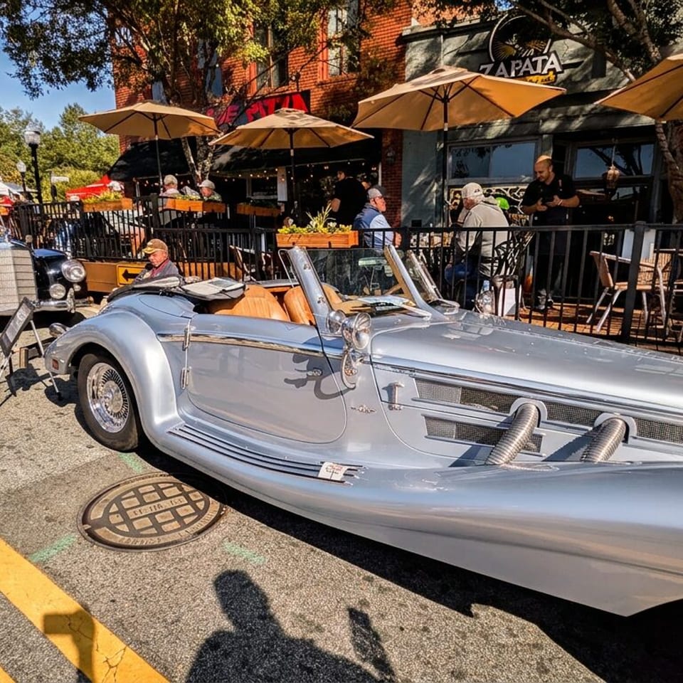 Vintage silver sports car parked outside Zapata restaurant, with a classic black car, patio umbrellas, and diners behind it.