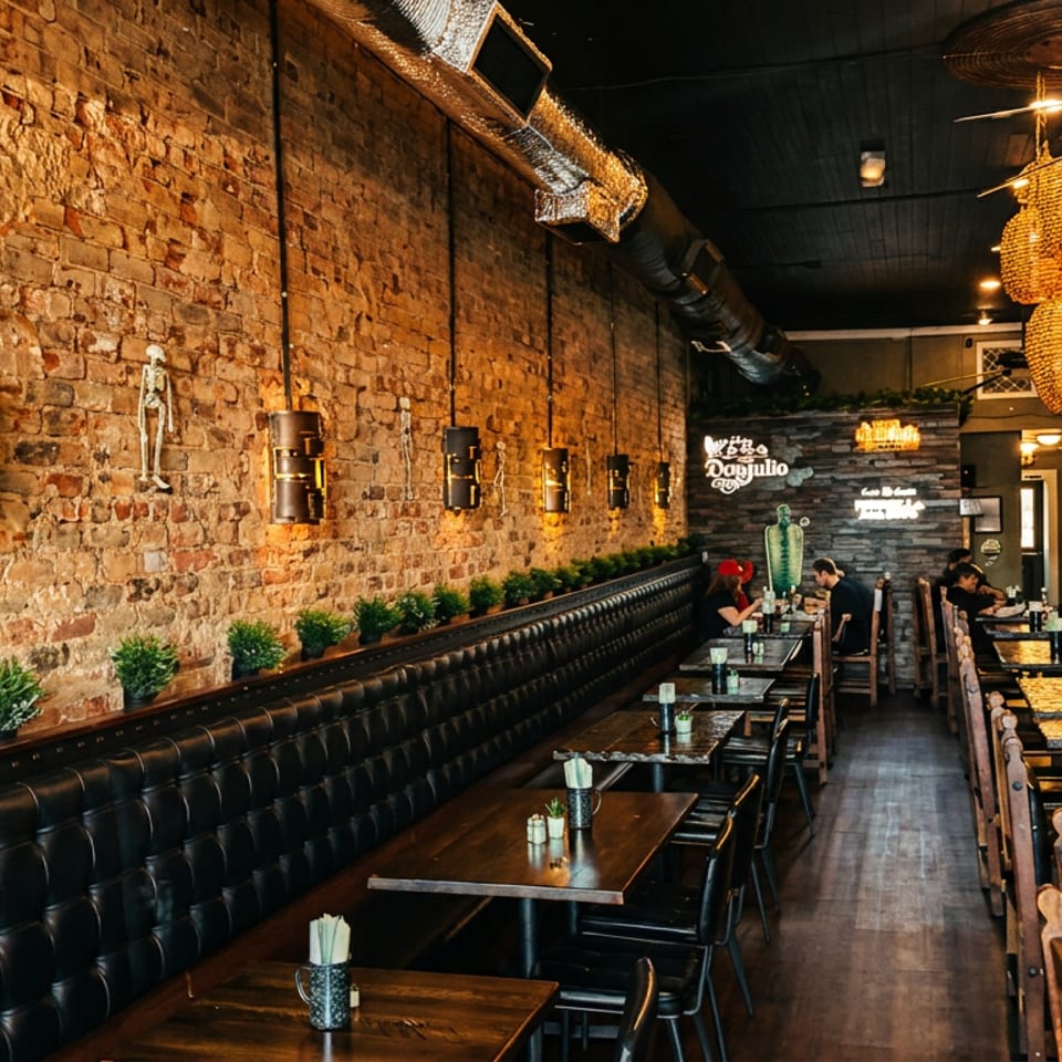 Warmly lit restaurant interior with exposed brick walls, leather banquette seating, wooden tables, hanging wicker lights, and diners.